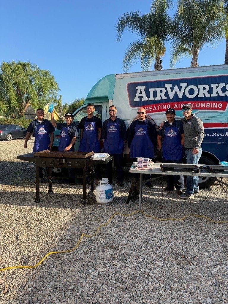 AirWorks technicians in aprons at a team cookout beside a branded service van